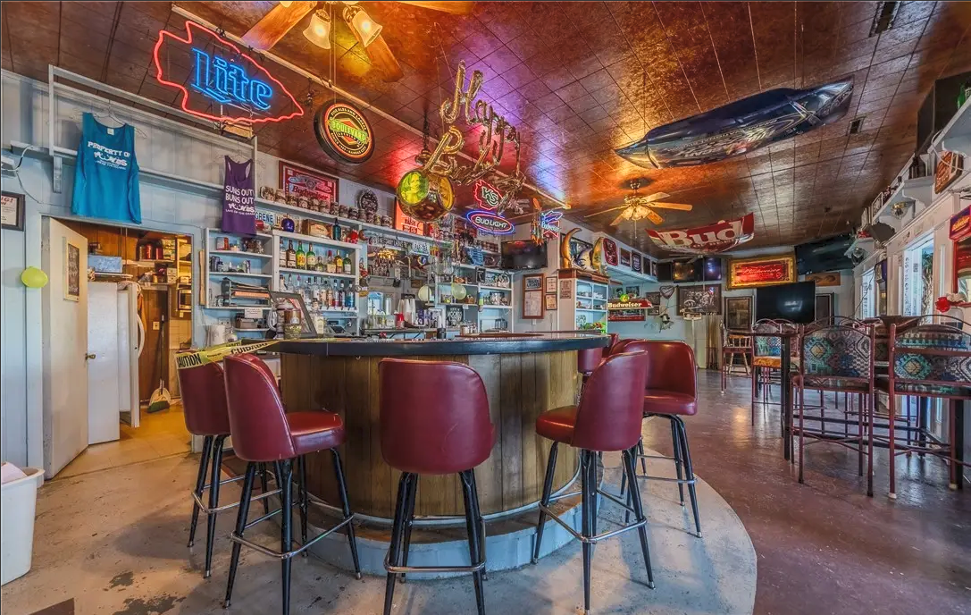 The horseshoe bar at Moonies, lit up with neon beer signs and lined with red barstools